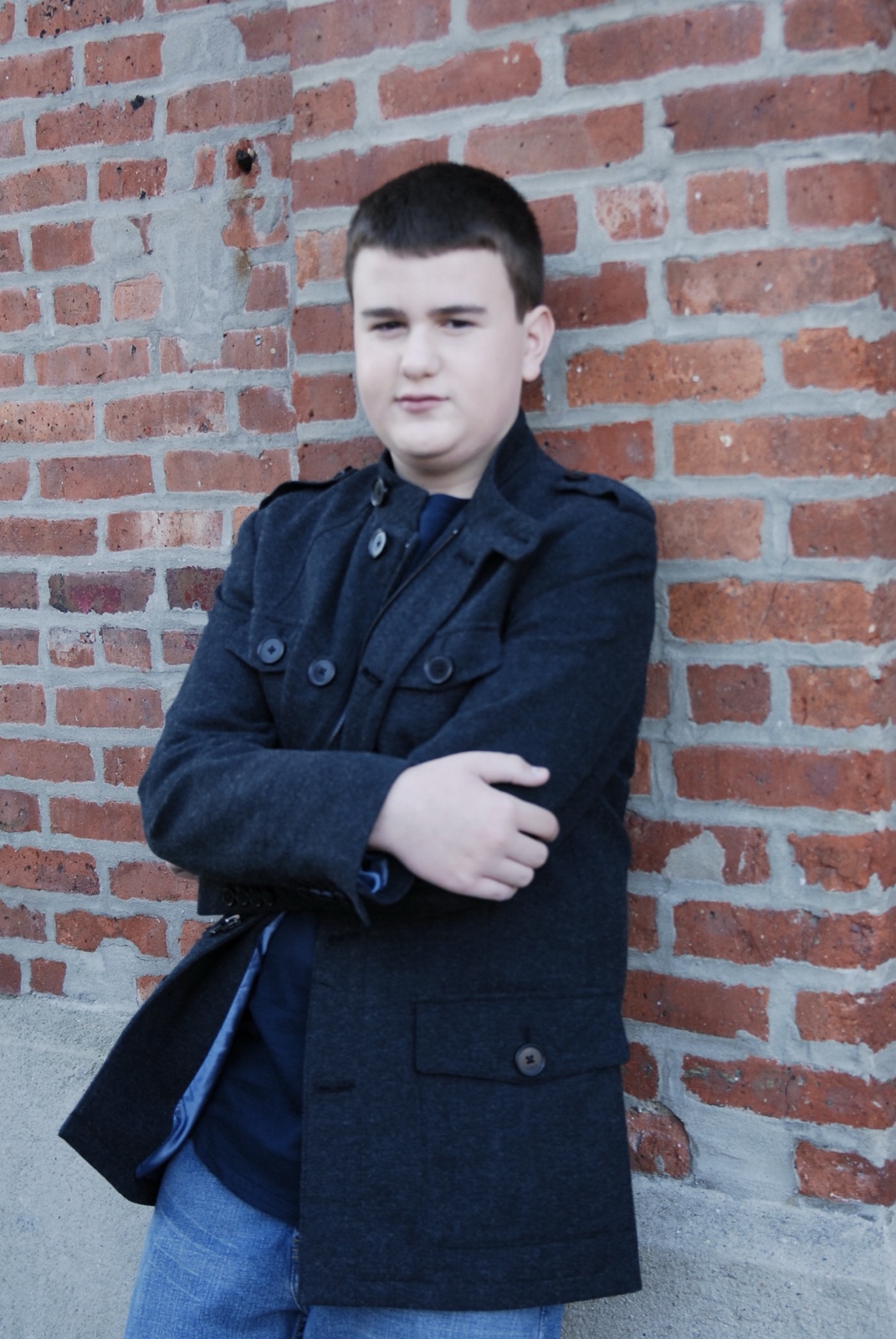 Matt McCabe as a kid in a dark peacoat, arms crossed, leaning against a red brick wall. Childhood acting press photo, circa 2009.