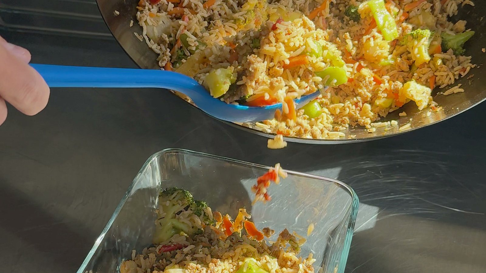A wok of finished ground turkey, rice, and vegetable meal prep being spooned into a glass meal-prep container.