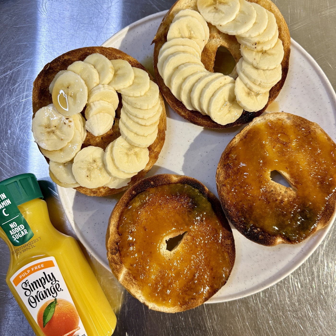 Race-morning breakfast: two plain bagels split into four halves and spread with jam, alongside a banana and a bottle of Simply Orange juice.